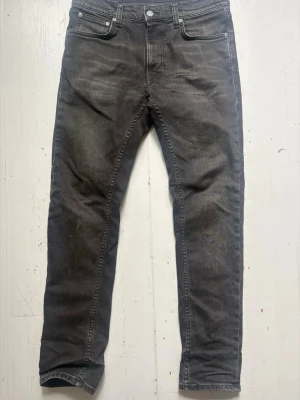 Nudie Jeans Lean Dean - Säljer ett par grå slim fit jeans med klassisk femficksdesign och diskreta slitningar. Jeansen har normal midja och raka ben, tillverkade i denim med lite stretch för skön passform. Perfekta för en avslappnad och trendig look. Storlek 29/30