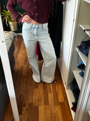Ljusblåa Wida jeans med hög midja - Säljer ett par ljusblå jeans med rak passform och hög midja. Jeansen har klassisk femficksdesign, gylf med knapp och dragkedja samt långa ben som faller snyggt över skorna. Perfekta för en avslappnad och trendig look.