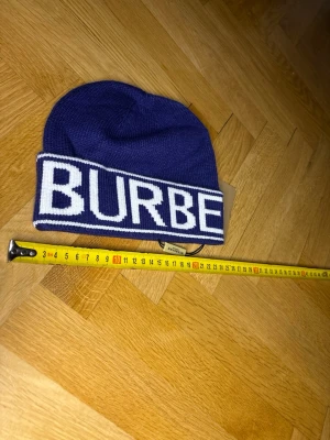 Blå mössa med vit text - Snygg blå mössa med bred vikt kant och stor vit text där det står'. Stickad i mjukt material och passar perfekt för kalla dagar. Klassisk modell som sitter skönt på huvudet och ger en trendig look.