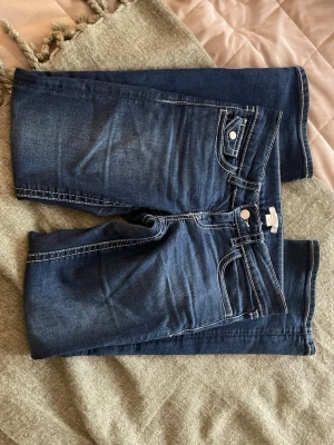 Mörkblå raka jeans med kontrastsömmar - Snygga mörkblå jeans med raka ben och tydliga kontrastsömmar. Klassisk femficksmodell med lock på ena bakfickan och silverfärgade detaljer. Jeansen är i ett mjukt denimtyg som passar perfekt till en avslappnad stil.