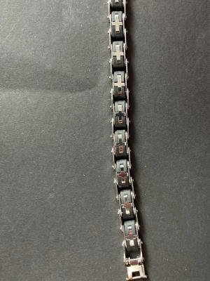 Svart och silverfärgat länkarmband - Snyggt armband i svart och silverfärgad metall med rektangulära länkar och korsliknande detaljer. Armbandet har en modern, industriell känsla och passar perfekt för dig som gillar stilrena accessoarer med edge.