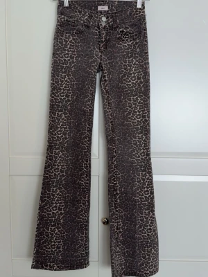 Bruna leopardmönstrade bootcut jeans - Säljer ett par bruna jeans med leopardmönster och bootcut-modell. Jeansen har klassisk femficksdesign, knappgylf och är tillverkade i ett stretchigt denimtyg. Perfekta för dig som vill sticka ut med ett djurmönster i garderoben.