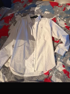 Vit skjorta från Gant - Klassisk vit skjorta från Gant med lång ärm och knappar framtill. Skjortan har en liten broderad logga på bröstet och är tillverkad i bomull. Perfekt för en stilren och clean look.