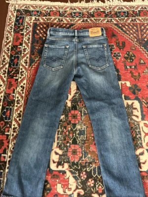 Blå jeans från Replay - Snygga blå jeans från Replay med klassisk femficksdesign och tydliga slitningar. Jeansen har raka ben och bakfickor med dekorativa sömmar. Perfekta för en avslappnad och trendig look.