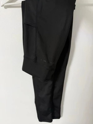 Svarta leggings med ficka - Säljer två par svarta leggings med praktisk ficka på sidan. De har en tight passform och är tillverkade i ett stretchigt material som sitter skönt på kroppen. Perfekta för träning eller chill dagar. De är köpta i lager 157. Ett par för 40kr eller två för 60