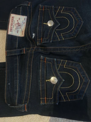 Mörkblå True Religion jeans bootcut - Säljer ett par mörkblå bootcut jenas fårn true religion, UPPSYDDA!  Lämnade in dem för de var för långa skriv hur lång du är om du är intresserad så kan jag se på min längd om dom passar!  Becca 