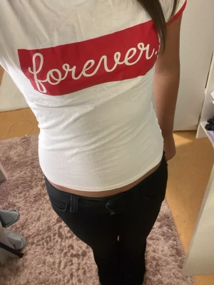Vit t-shirt med röd text forever - Säljer en vit t-shirt med röd kant vid ärmar och hals samt ett rött tryck med texten 'forever' på bröstet. T-shirten har en tight passform och är kortärmad, perfekt för dig som gillar enkel men snygg stil.