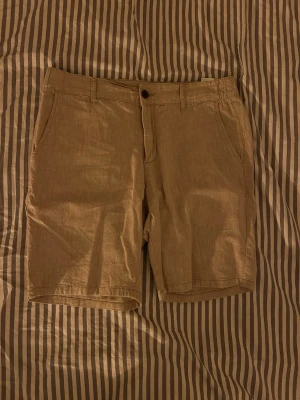 Beige linneshorts i bomullsblandning - Snygga beige shorts i en skön blandning av linne och bomull. Klassisk passform med fickor på sidorna och hällor för bälte. Perfekta för varma dagar och enkel att matcha med olika toppar.