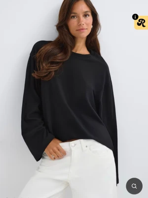 Svart långärmad topp med loose fit - En svart långärmad topp med avslappnad, loose passform och rund halsringning. Toppen är enkel och stilren, perfekt att matcha med jeans eller kjol. Materialet ser ut att vara mjukt och bekvämt, troligen bomull eller polyester.