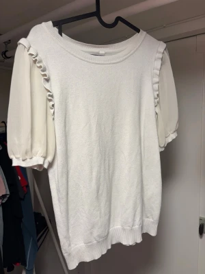 Vit topp med volang från Soyaconcept - Supersöt vit topp från Soyaconcept med puffiga korta ärmar och volangdetaljer längs axlarna. Rund halsringning och ribbade muddar nedtill ger en chill och trendig look. Perfekt till jeans eller kjol för en fräsch outfit. Står inte vilken storlek men passar mig bra som har S!❣️