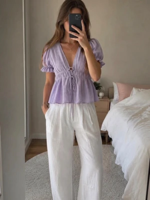 Ljuslila blus med puffärm och knyt - Supersöt ljuslila blus med puffärmar, v-ringning och knyt i midjan. Blusen har en lätt volang nedtill och resår vid ärmsluten för en feminin look. Perfekt till både jeans och kjol för en trendig stil. Aldrig använd & i nyskick. 