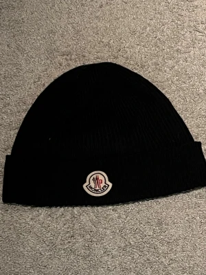 Svart Moncler mössa  - En riktigt fett svart moncler mössa! Väldigt säker på att det är en modell från 2022 så rätt så gammal modell. Men ändå rätt så bra skick eftersom den inte är använd så mycket! Säljer för 700 kr men kan gå med på priser ner till 500 kr möjligtvis kanske ännu mer vid snabbt köp!!
