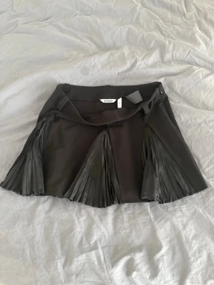 Svart kjol med plisserade detaljer Weekday - Säljer en svart kjol från Weekday i storlek 36. Kjolen har  plisserade paneler som ger en cool och trendig look. Materialet är mjukt och följsamt, använd 1 gång. Storleken passar 36-38. 