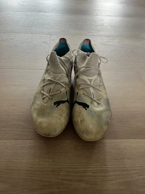 Puma fotbollsskor med snörning - Säljer ett par fotbollsskor från Puma med svart logga på ovansidan. Skorna har snörning, låg profil och stickad ovandel för bra passform. Yttersulan är ljus med inslag av rosa. Perfekta för dig som vill ha stilrena och funktionella skor på planen.