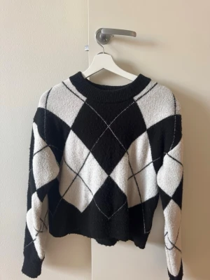 Svartvit stickad tröja Gina Tricot - Stickad tröja från Gina Tricot i svart och vitt med stort rutmönster. Tröjan har rund halsringning och ribbade muddar vid hals, ärmslut och nederkant. 