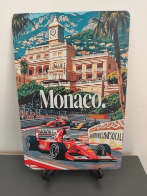 Monaco plåtskylt med Formel 1-motiv - Snygg plåtskylt med färgglatt motiv från Monacos Formel 1-bana. Skylten visar klassiska racingbilar framför en ikonisk byggnad och palmer, med texten 'Monaco' i vitt. Perfekt för motorsportfans eller som dekoration i rummet.