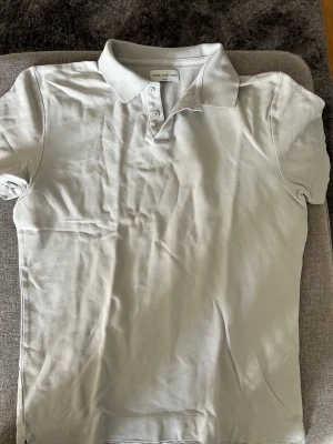 Ljusgrå pikétröja These Glory Days - Säljer en stilren ljusgrå pikétröja från These Glory Days i bomull. Tröjan har klassisk krage, korta ärmar och knappar framtill. Perfekt till jeans eller shorts för en clean look.
