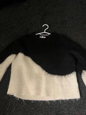 Svartvit stickad tröja med vågig design - Säljer en stickad tröja i svart och vitt med en cool vågig färgövergång. Tröjan har lång ärm, rund halsringning och är gjord i ett mjukt, fluffigt material som känns riktigt mysigt. Perfekt för dig som gillar en unik och trendig look.