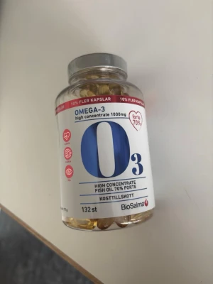 Omega-3 kosttillskott BioSalma - Burk med 132 kapslar Omega-3 kosttillskott från BioSalma. Högkoncentrerad fiskolja, 1000 mg per kapsel och 70% forte. Burken är genomskinlig med silverfärgat lock och etikett i vitt, blått och rött.
