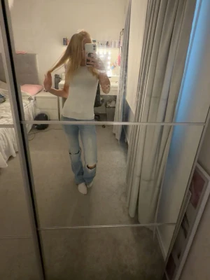 Ljusblå nelly jeans - Säljer ett par ljusblå nelly jeans med hål på knäna. Jeansen har en avslappnad passform och är perfekta för en trendig och casual look. Materialet är klassisk denim i bomull. De har en liten klorin fläck på låret men inget man tänker på i dags ljus.