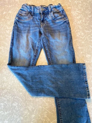 Blå low waist jeans från Gina Tricot - Säljer ett par klassiska blå bootcut jeans från Gina Tricot. Jeansen har fem fickor, bälteshällor och knappgylf. Materialet är slitstarkt denim i bomull och passformen är något utsvängd nedtill. Perfekta till en avslappnad och trendig look.
