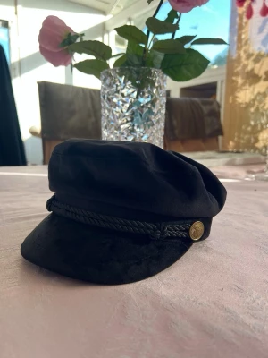 Svart skepparmössa - Stilren svart skepparmössa från Gina Tricot med dekorativt snöre och guldfärgade knappar på sidorna. Tror aldrig den är använd🫶🏻 skriv för mer frågor💗