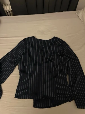 Mörkblå blus med vita ränder - snygg svart blus med tunna vita vertikala ränder och långärmad design. blusen har en asymmetrisk nederkant och markerad midja.