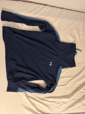 Blå tröja  från Under Armour - Säljer en mörkblå träningströja från Under Armour i  L/G. Perfekt för träning, löpning eller en sportig vardagsstil. Bekvämt material som ger bra rörelsefrihet och passar bra både på gymmet och till vardags. Tröjan är i fint skick.