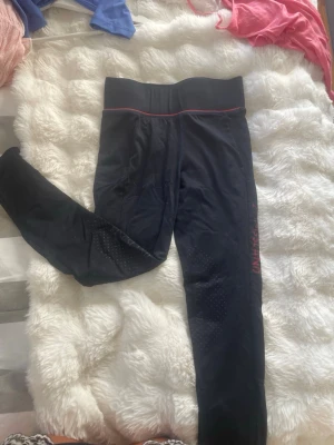 Svarta ridtights från Kingsland - Säljer ett par svarta ridtights från Kingsland med hög midja och diskreta prickdetaljer på benen för extra grepp. Tightsen har en röd logga längs benet och är tillverkade i ett stretchigt funktionsmaterial som passar perfekt till träning.