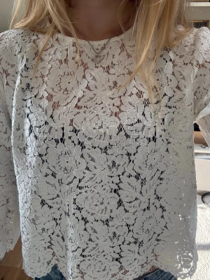 Vit spetsblus med blommönster - Säljer en vit blus i spets med detaljerat blommönster. Blusen har rund halsringning och långa ärmar med lätt puff vid axlarna. Materialet är genombrutet och ger en romantisk vibe. Perfekt att styla med jeans eller kjol för en trendig look.