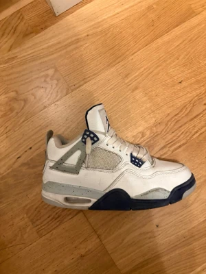 Vita och blåa jorden 4  - Snygga vita sneakers med marinblå och grå detaljer. Skorna har meshpaneler på sidorna, synlig luftdämpning i sulan och coola plastdetaljer vid snörningen. Perfekta för dig som gillar streetwear och sportig stil.
