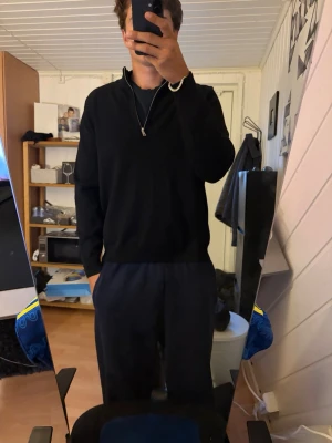 Svart halvzip tröja med hög krage - Säljer en svart långärmad tröja med halvzip och hög krage. Tröjan har en clean och enkel design utan synliga loggor eller mönster. Perfekt för dig som gillar en stilren look. Materialet ser ut att vara mjukt och bekvämt, troligen bomull eller bomullsblandning. Storleken är xl men sitter som L/M