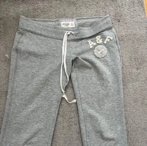 Abercrombie and fitch mjukisbyxor - Snygga grå mjukisbyxor med dragsko i midjan och broderad A&F-logga på vänster sida. Byxorna har bred mudd i midjan och är tillverkade i mjukt sweatshirtmaterial. Perfekta för chill dagar eller när du vill vara bekväm men ändå se fräsch ut.