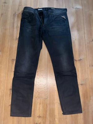 Svarta Replay Anbass slim fit jeans  - Säljer ett par svarta slim fit jeans från Replay av modellen Anbass med diskreta slitningar och klassisk femficksmodell. Jeansen har en liten Replay-logga vid fickan och är tillverkade i ett mjukt, stretchigt material för extra komfort.  W36. L32. Nypris:1699kr.    Mitt pris:829kr