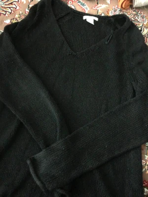 Svart stickad tröja med V-ringning - En enkel och stilren svart stickad tröja med V-ringning och långa ärmar. Tröjan har en klassisk passform och är perfekt att matcha med jeans eller kjol. Tillverkad i mjukt stickat material för en bekväm känsla.