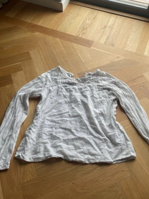 Vit långärmad basic blus med detaljer - Säljer en vit blus med långa ärmar och fina veckade detaljer vid axlar och halsringning. Blusen har en avslappnad passform och är tillverkad i ett tunt, mjukt tyg som känns luftigt och skönt.