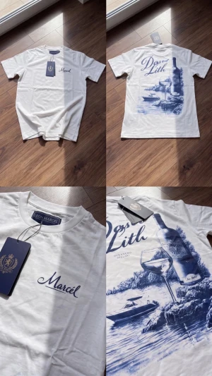 Vit t-shirt med blått tryck från CAIN - Vit t-shirt från CAIN med blått tryck framtill och stort konstnärligt motiv på ryggen. Motiv med flaska, glas och havsmiljö. Rund halsringning och normal passform. Perfekt för dig som gillar unika prints och stilrena detaljer.