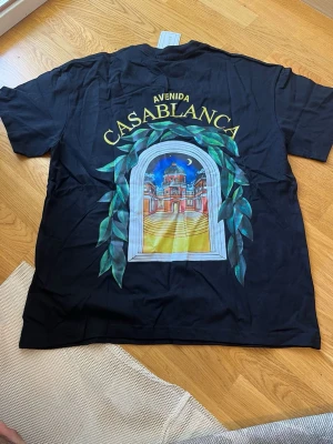 Svart Casablanca t-shirt med tryck - Snygg svart t-shirt från Casablanca med färgglatt tryck av ett fönster och byggnad på både bröstet och ryggen. T-shirten har rund hals och korta ärmar. Perfekt för dig som vill sticka ut med en unik design.
