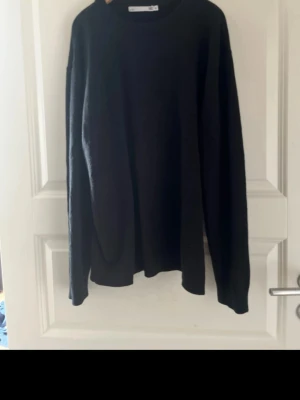 Svart stickad tröja med rund hals - En stilren svart stickad tröja med rund hals och långa ärmar. Perfekt för lager-på-lager och enkel att matcha med olika outfits. Tröjan har en klassisk passform och är mjuk och bekväm att bära.