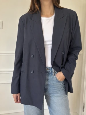 H&M mörkblå dubbelknäppt blazer – stl S - Stilren mörkblå blazer från H&M i storlek S. Dubbelknäppt modell med slag, långa ärmar och fickor framtill. Rak och något oversized passform som är fin både till jeans och över klänning eller kostymbyxor.