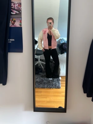 Rosa och vit bomberjacka Juicy Couture - Snygg bomberjacka från Juicy Couture i ljusrosa med vita ärmar. Jackan har broderad logga fram och texten 'Juicy Couture' i rosa på ryggen. Klassisk bombermodell med ribbade muddar och krage. Perfekt för en trendig och avslappnad look.