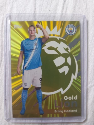 Topps Gold Lion Erling Haaland kort - Samlarobjekt: Topps Gold Lion fotbollskort med Erling Haaland från Manchester City, säsong 2025/26. Kortet har en glansig guldfärgad bakgrund med Premier League-loggan och levereras i plastficka.
