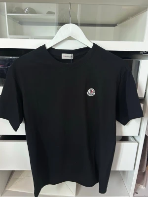 Moncler t-shirt  - Snygg svart t-shirt från Moncler med klassisk rund hals och liten broderad Moncler-logga på bröstet. Tillverkad i mjuk bomull och har en enkel, stilren design som passar till det mesta.
