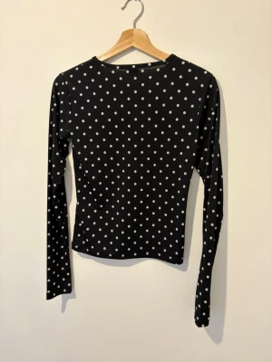 Svart prickig långärmad topp Gina Tricot - Snygg svart långärmad topp från Gina Tricot med vita prickar. Toppen har en rund halsringning och är figurnära i modellen. Perfekt att styla med jeans eller kjol för en trendig look.