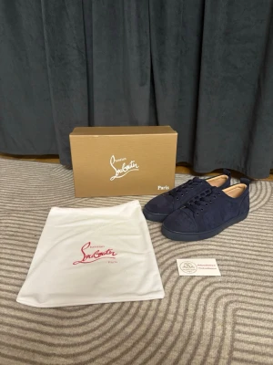 Mörkblå sneakers från Christian Louboutin - Snygga mörkblå sneakers från Christian Louboutin i mocka med klassiska röda sulor och ton-i-ton snörning. Skorna har en stilren och låg profil som passar till många olika outfits. Levereras med originalkartong och dustbag.