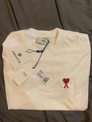 Vit t-shirt från Ami med rött hjärta - Snygg vit t-shirt från Ami med det ikoniska röda hjärta-A broderiet på bröstet. Klassisk rund halsringning och mjukt bomullsmaterial. Perfekt för en clean och stilren look.