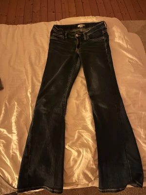 Mörkblå bootcut jeans med kontrastsömmar - Säljer ett par mörkblå bootcut jeans med snygga kontrastsömmar och klassisk femficksdesign. Jeansen har utsvängda ben och är tillverkade i ett mjukt denimtyg som sitter skönt. Perfekta för dig som gillar retrovibbar och vill ha ett par jeans som sticker ut och sköna att ha på sig💕