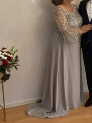 Silverfärgad långklänning med paljetter - Elegant silverfärgad långklänning med glittriga paljetter och fjäderdetaljer på ärmarna. Perfekt för en glamorös kväll. Den har litet kort släp. Nypris: 6000kr använd 1 gång, dragkedja på ryggen. Storlek 46/48