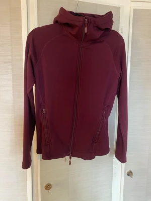 Vinröd hoodie med dragkedja - Snygg vinröd hoodie med hel dragkedja framtill och två fickor med dragkedja. Hoodien har en åtsittande huva och långa ärmar. Använd en gång så i nyskick