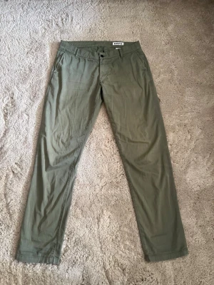 Chinos från HOPE - Snygga olivgröna chinos från HOPE. Liten slitning vid höger bakficka. Skriv vid funderingar